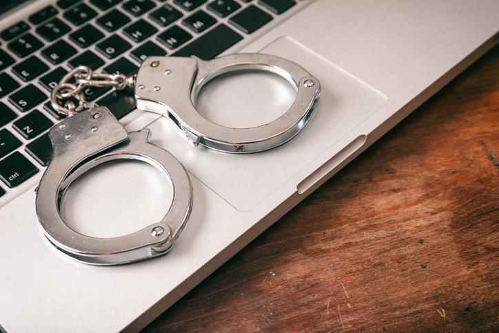 Handcuffs on a computer on a wooden background.